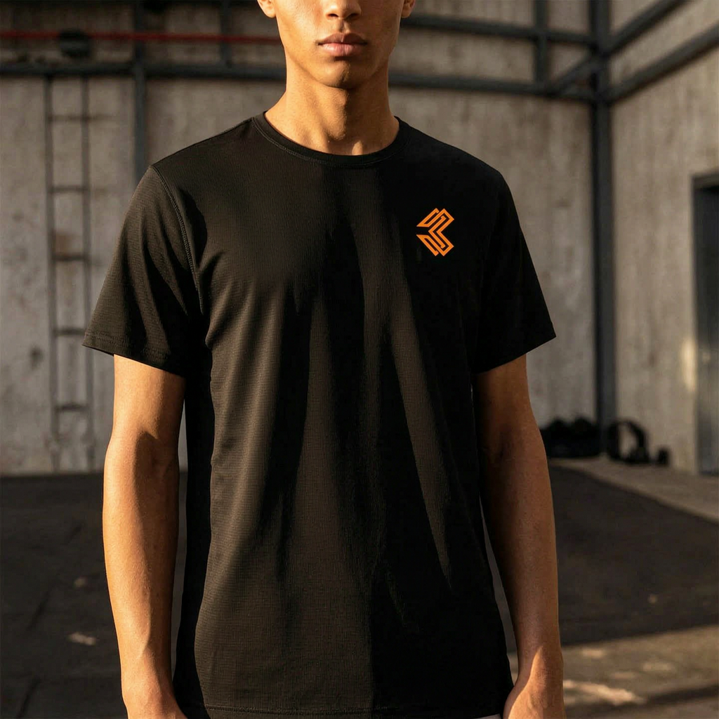 Liga Combat Rounds Training Tee worn in a gym, black training tee with the orange chest mark