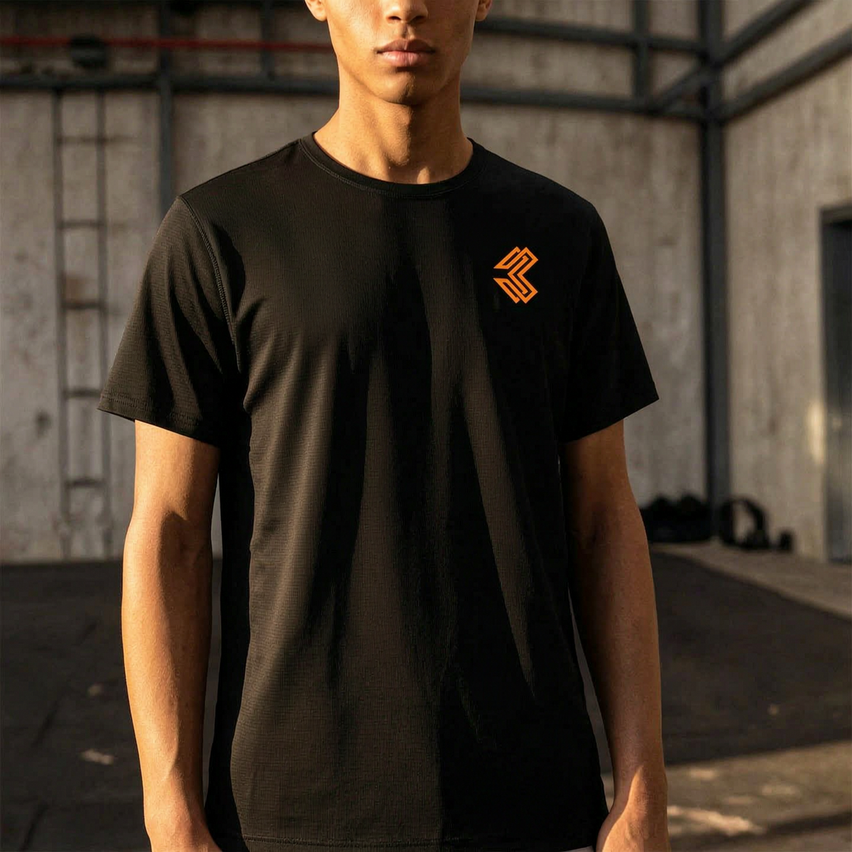 Liga Combat Rounds Training Tee worn in a gym, black training tee with the orange chest mark