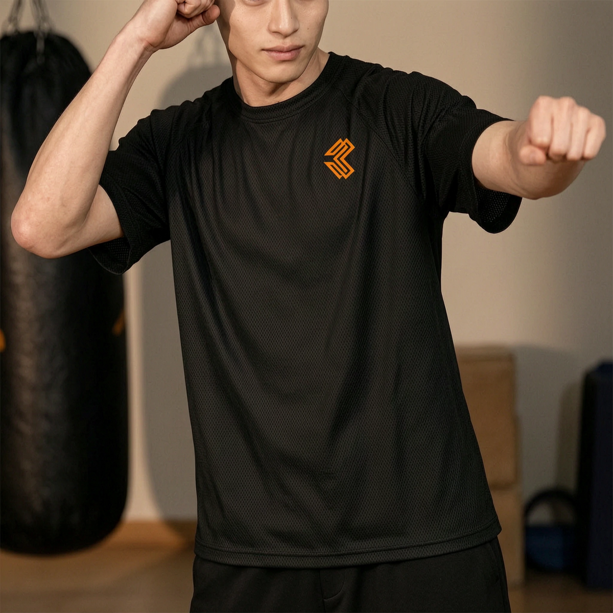 Liga Combat Rounds Mesh Tee in black, worn shadow boxing by the heavy bag, orange chest monogram visible