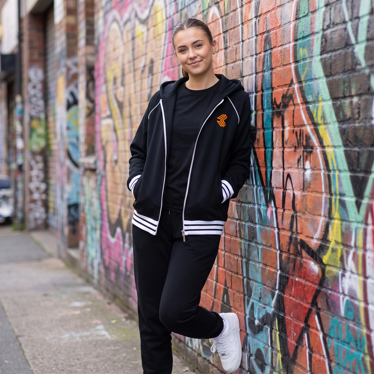 Liga Combat Varsity Mantra Jacket in black worn open against a graffiti wall, street style