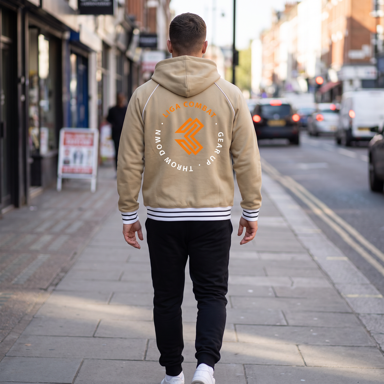 Liga Combat Varsity Mantra Jacket in khaki from behind on a city street, circular back crest