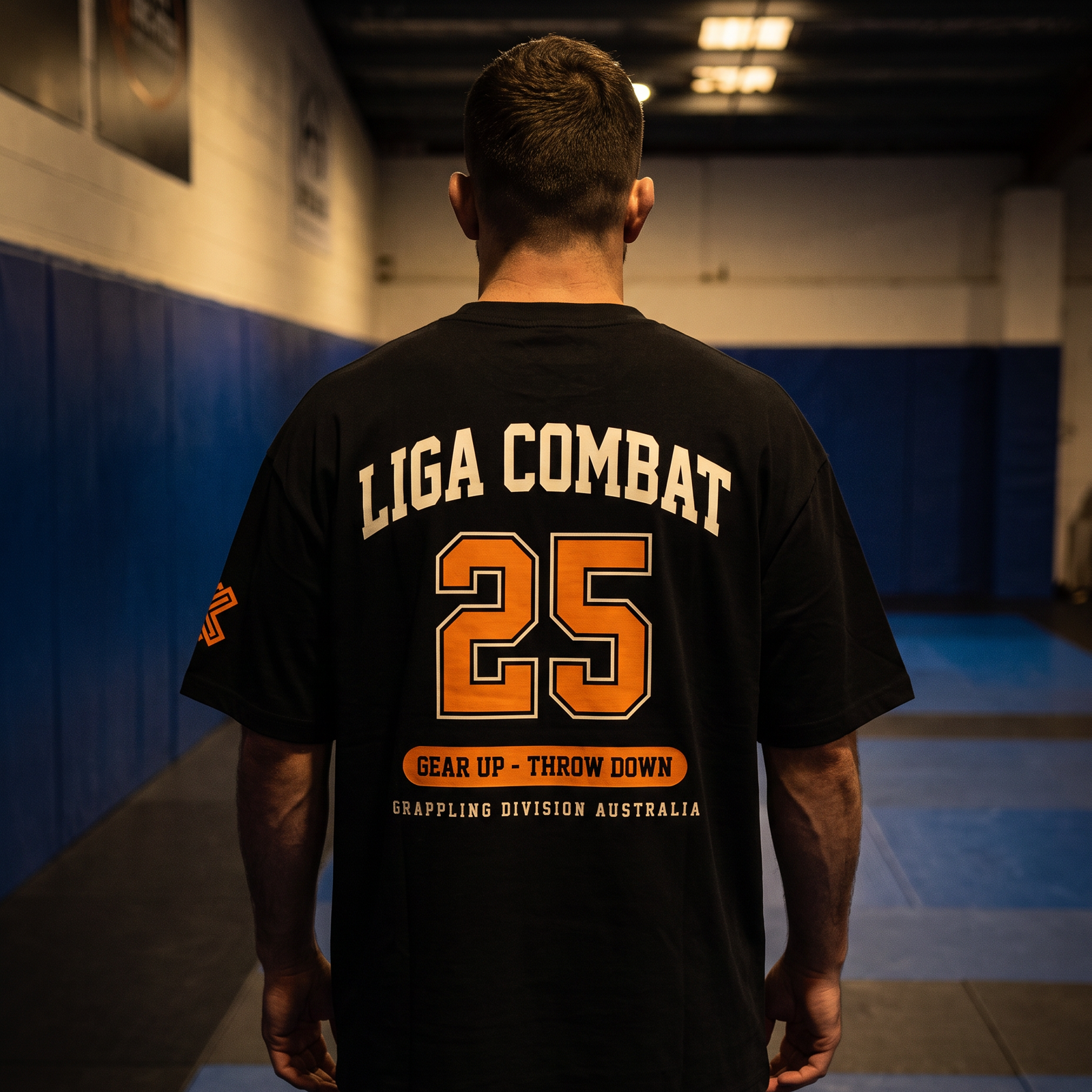 Liga Combat Varsity 25 Tee worn back-on in the gym, full collegiate print visible
