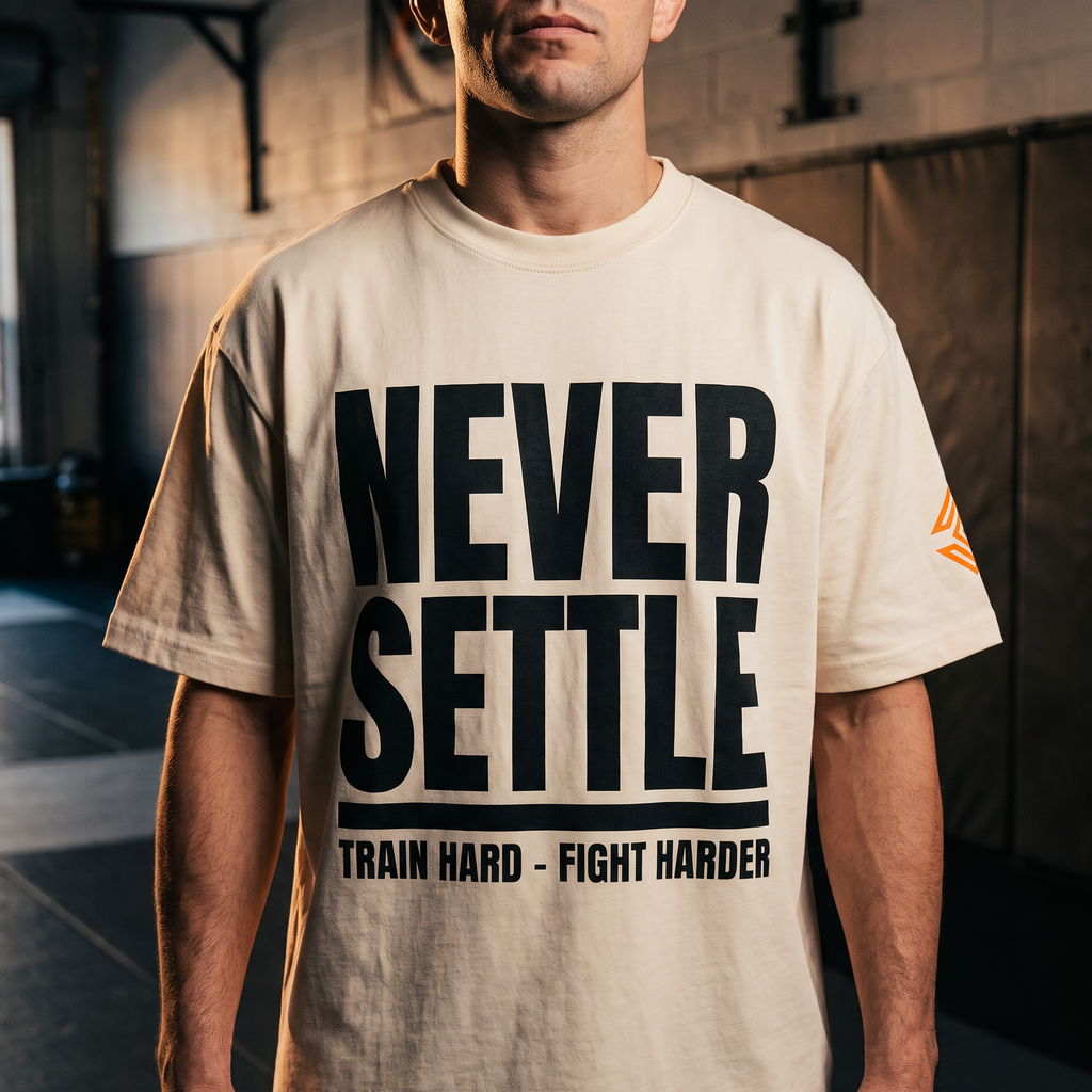 Liga Combat Never Settle Tee in natural cream worn front-on in the gym, full black statement print visible