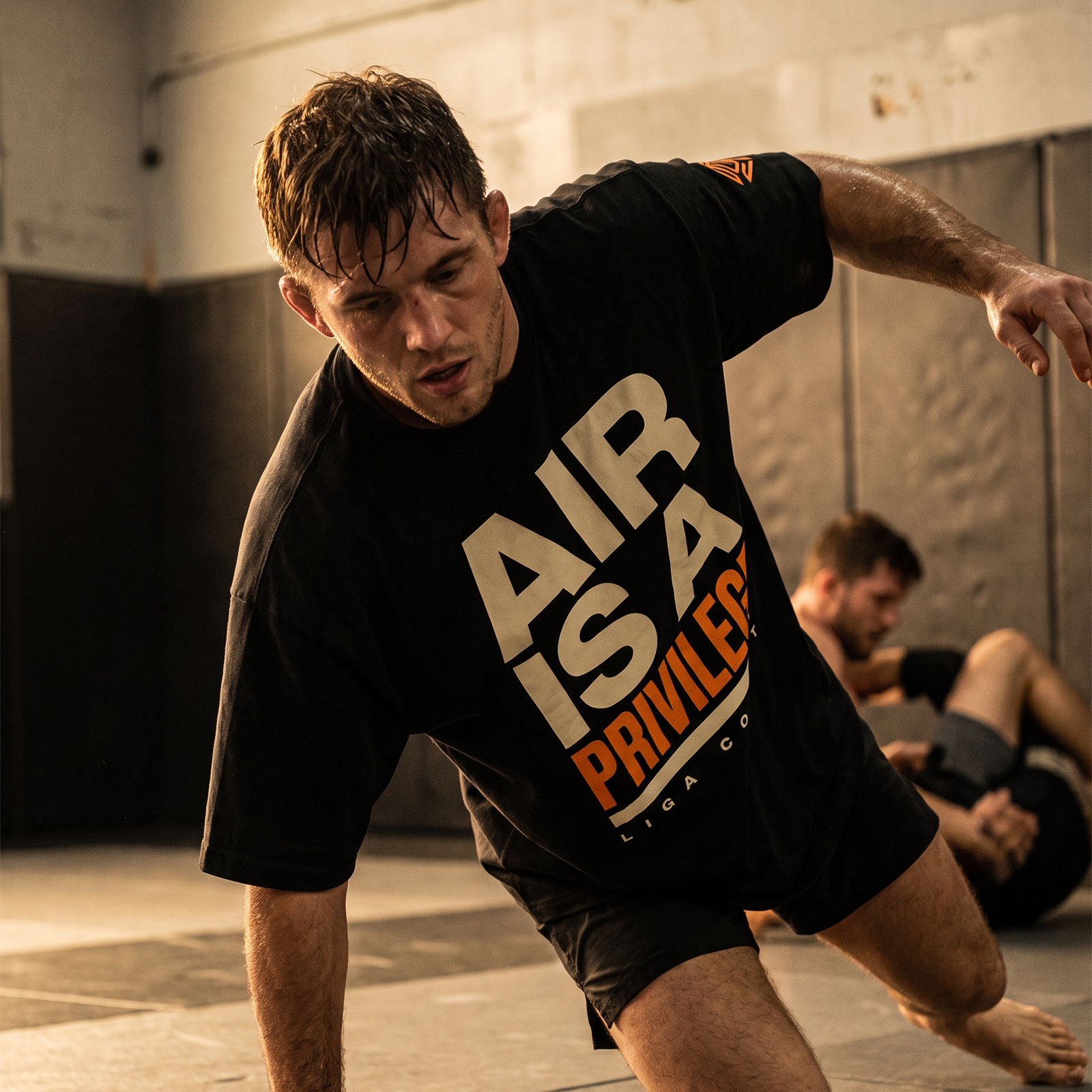 Grappler in the Liga Combat Air Is A Privilege Tee rising off the mat mid-motion after a hard round