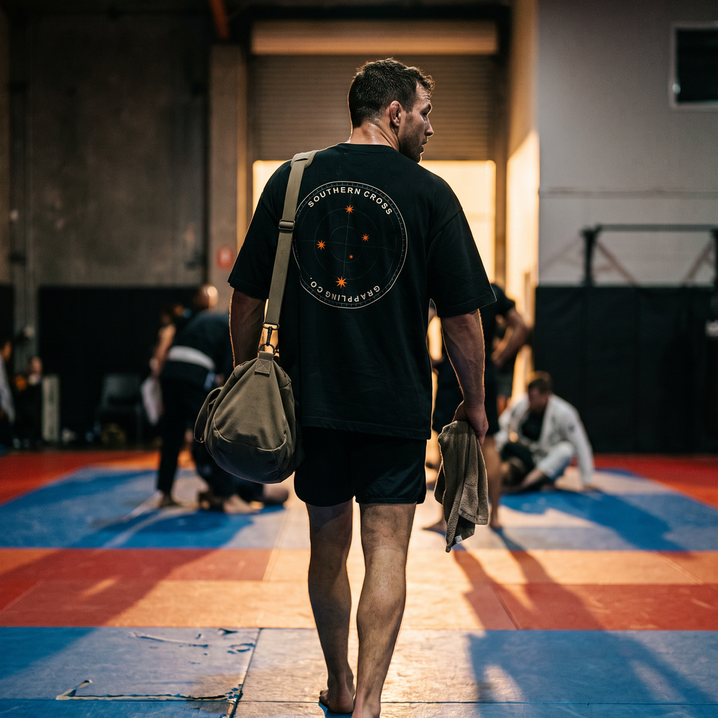 Grappler in the Liga Combat Southern Cross Grappling Tee walking off the mats after training, bag in hand