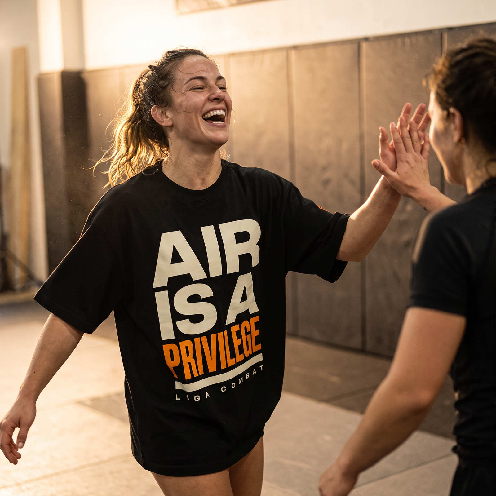 Woman in the Liga Combat Air Is A Privilege Tee laughing and high-fiving a training partner after a round
