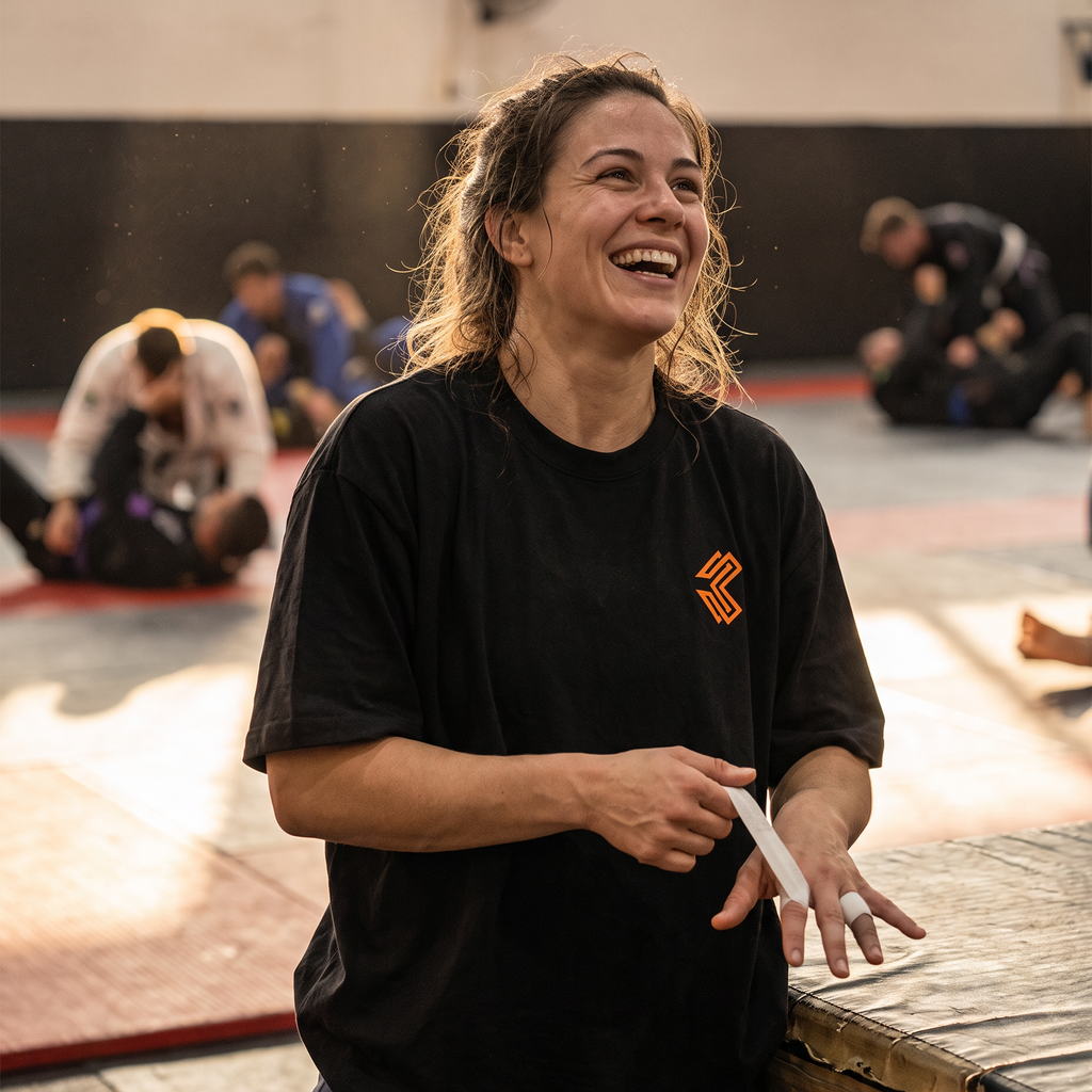 Woman in the Liga Combat Gentle Art Terms Tee taping her fingers mat-side, laughing before training