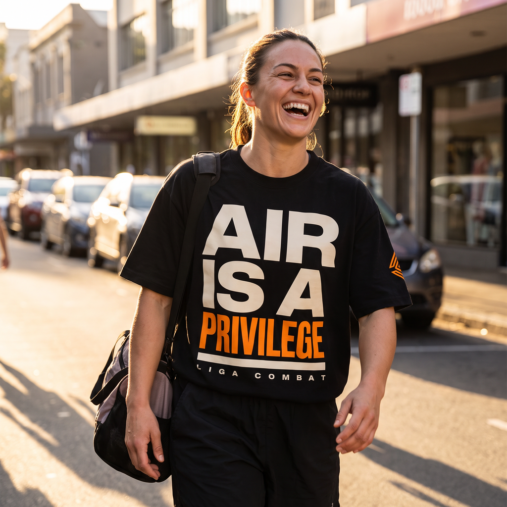 Woman wearing the Liga Combat Air Is A Privilege Tee walking a city street at golden hour, gym bag on shoulder