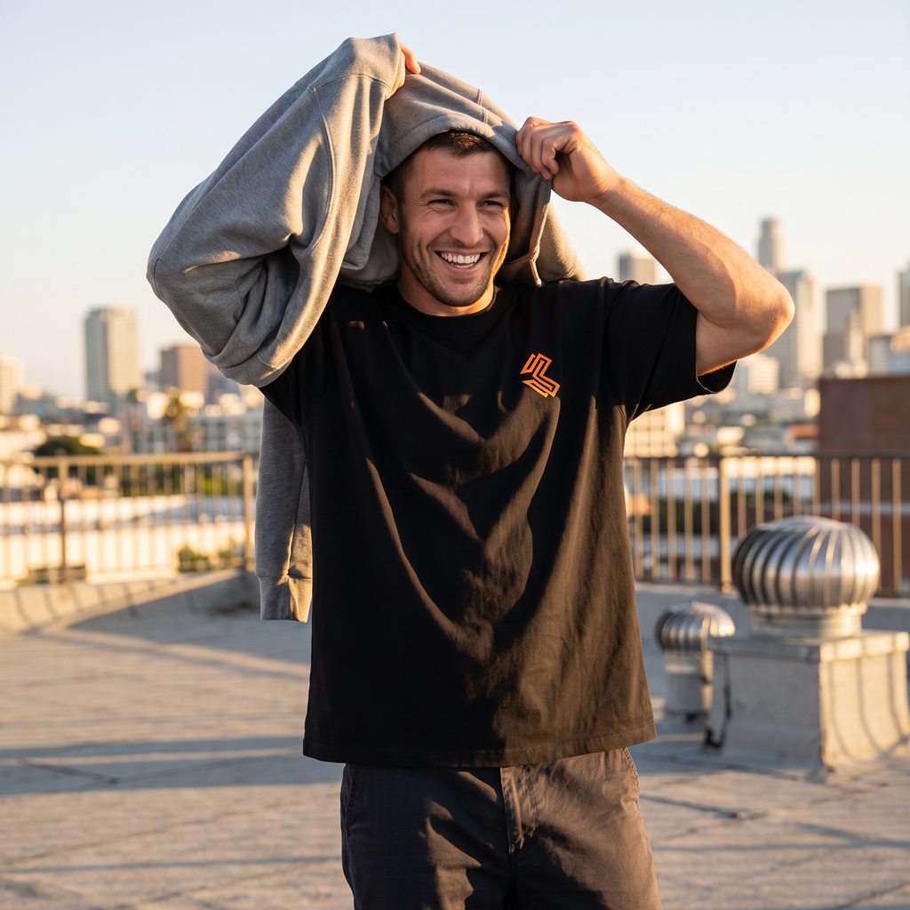 Man in the Liga Combat Gentle Art Terms Tee pulling a hoodie off on a rooftop at golden hour