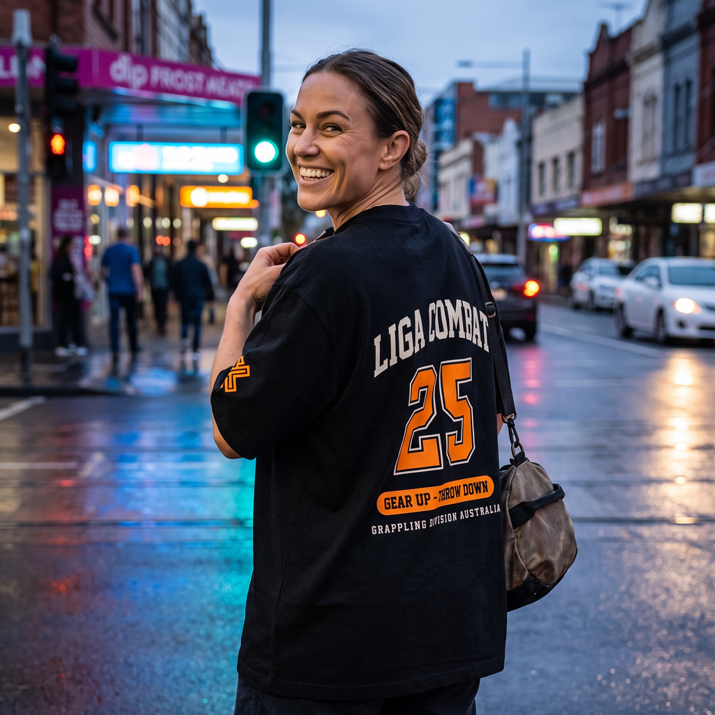 Woman in the Liga Combat Varsity 25 Tee on a city street at dusk, looking back over her shoulder