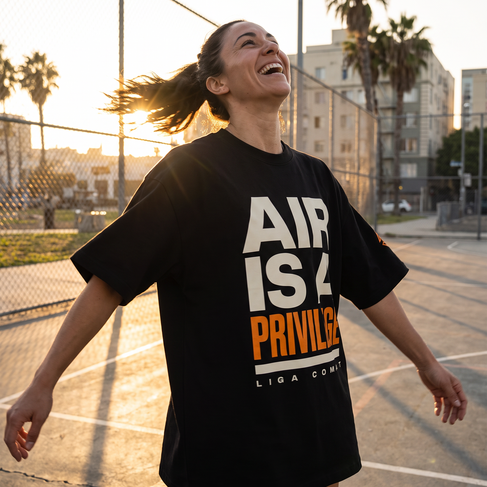 Woman in the Liga Combat Air Is A Privilege Tee spinning mid-step on a city basketball court at sunset