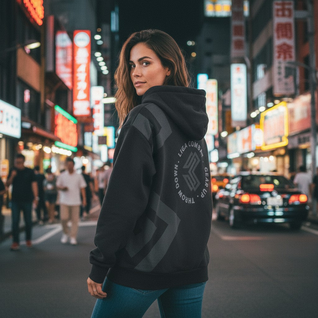 Woman wearing a black Liga Combat Blackout Emblem hoodie with a circular logo on the back in a busy city street