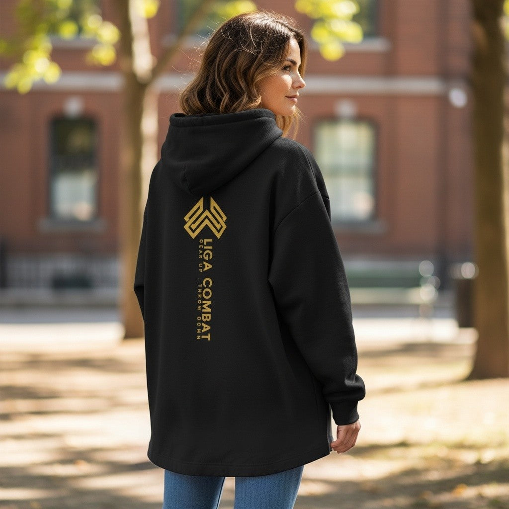 Woman wearing a black Liga Combat Throwdown Emblem hoodie with a gold logo on the back in an outdoor park setting
