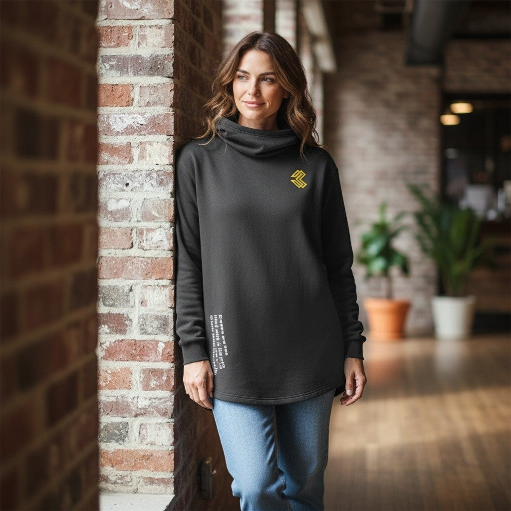 Woman wearing a black Liga Combat Throwdown Emblem hoodie with a cowl neck and yellow logo, leaning against brick wall