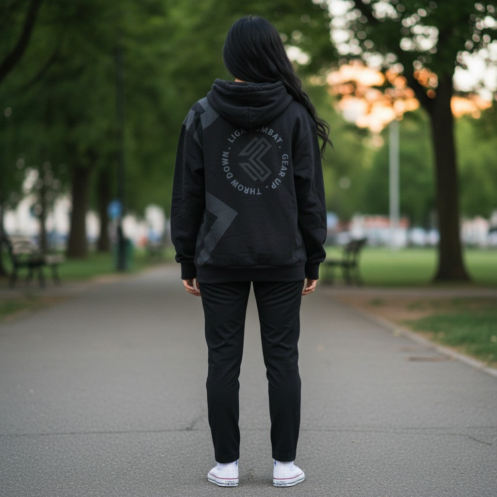 Woman wearing a black Liga Combat Blackout Emblem hoodie with a circular logo on the back, viewed from behind.