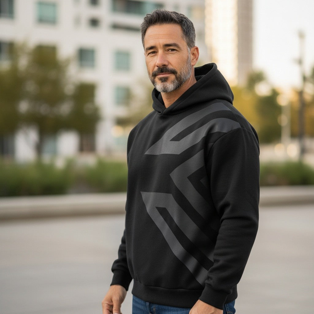 A man wearing a Liga Combat Blackout Emblem hoodie with a subtle dark geometric print in an urban outdoor setting.